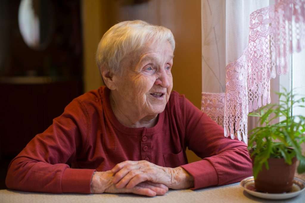 Elderly woman looks out the window sitting at the table.